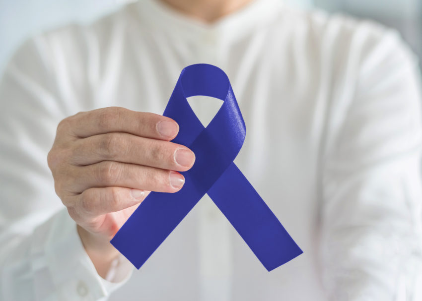 Colorectal Colon cancer awareness ribbon for men's health care concept with blue bow color in person's hand