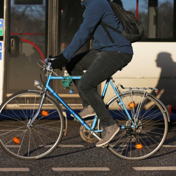 Person riding bicycle in bike lane near bus in a urban area.