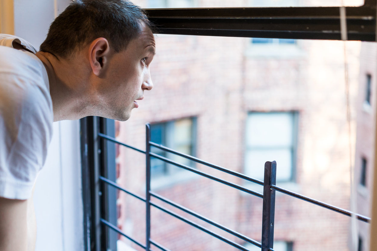 latino man in home housing apartment looking out window amid coronavirus pandemic