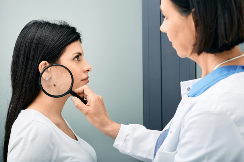 Doctor examining woman's neck with mole or birthmark using magnifying glass