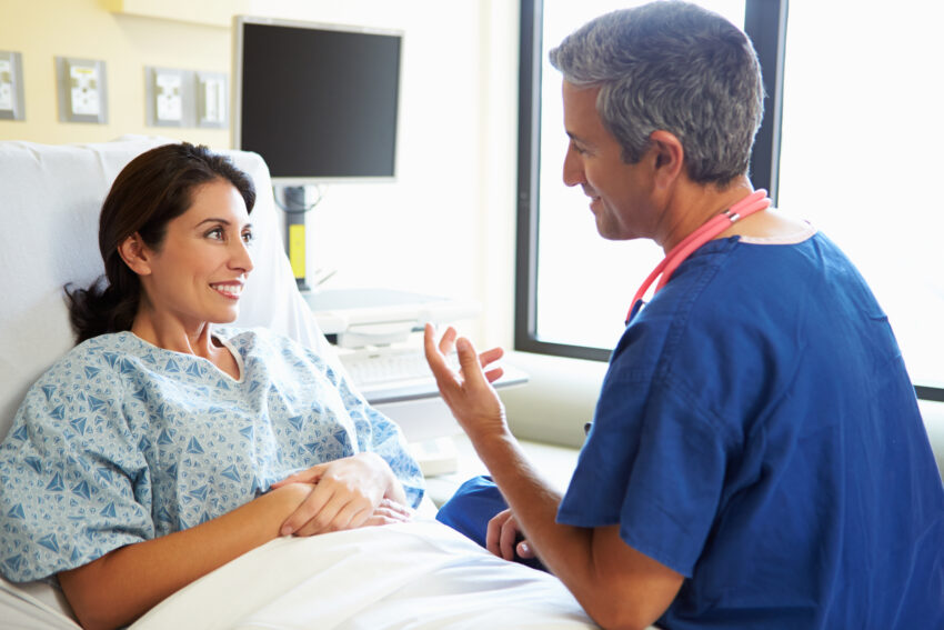 Male Nurse Talking With Female Patient In Hospital Room