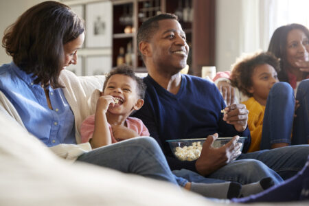 Three generation family family sitting on the sofa in living room, watching TV and eating popcorn