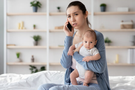 Worry Young Mother Holding Newborn Baby On hands And Talking On Cellphone