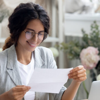 Head shot smiling young businesswoman reading paper with banking loan approval notification.