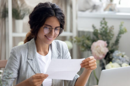 Head shot smiling young businesswoman reading paper with banking loan approval notification.