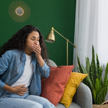 Young beautiful hispanic woman sick at home sitting on sofa with nausea and stomach ache