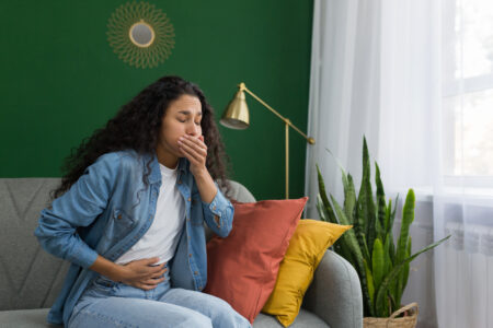 Young beautiful hispanic woman sick at home sitting on sofa with nausea and stomach ache