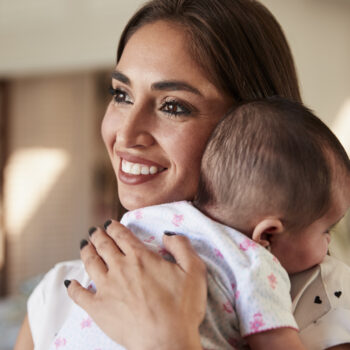 Smiling millennial mother holding her newborn son close to her chest, head and shoulders, close up