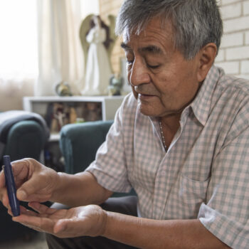 Elderly adult with diabetes pricking a finger to draw blood to measure his sugar levels from home