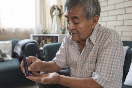 Elderly adult with diabetes pricking a finger to draw blood to measure his sugar levels from home