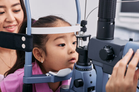 Checking little girl's eyesight with binocular slit lamp in ophthalmology clinic, close-up. Vision correction in children