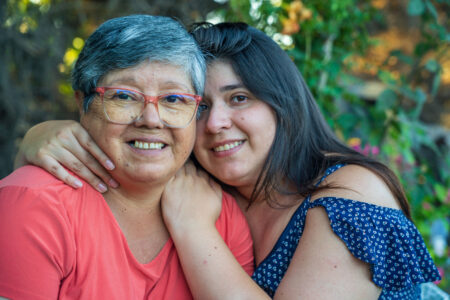 A young woman is warmly embracing an older woman who wears stylish glasses, showcasing a heartwarming moment filled with affection