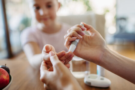 other checking girl's blood glucose level using a fingerstick glucose meter.