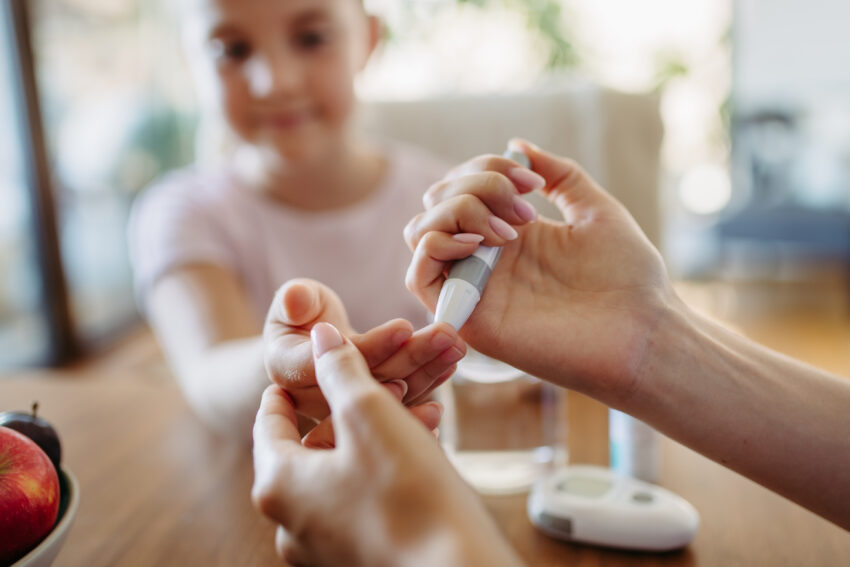 other checking girl's blood glucose level using a fingerstick glucose meter.