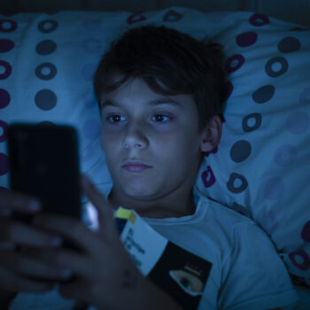 Child in bed at night with a book and a smartphone in the dark. Concept of problems with mobile addiction at young ages. Child with sleeping problems and insomnia due to the use of electronic devices