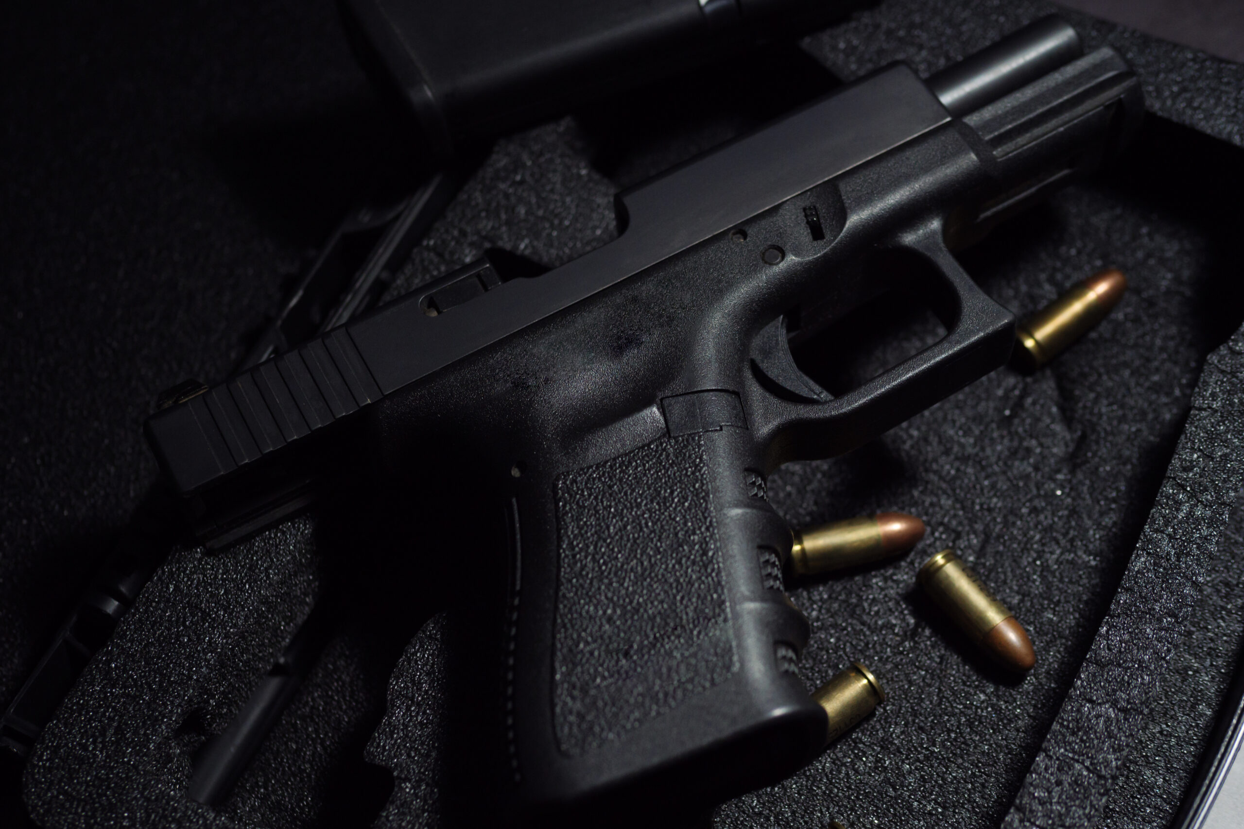 Close-up of two black metal 9mm automatic pistols with bullets all resting on a gun case against a black background.