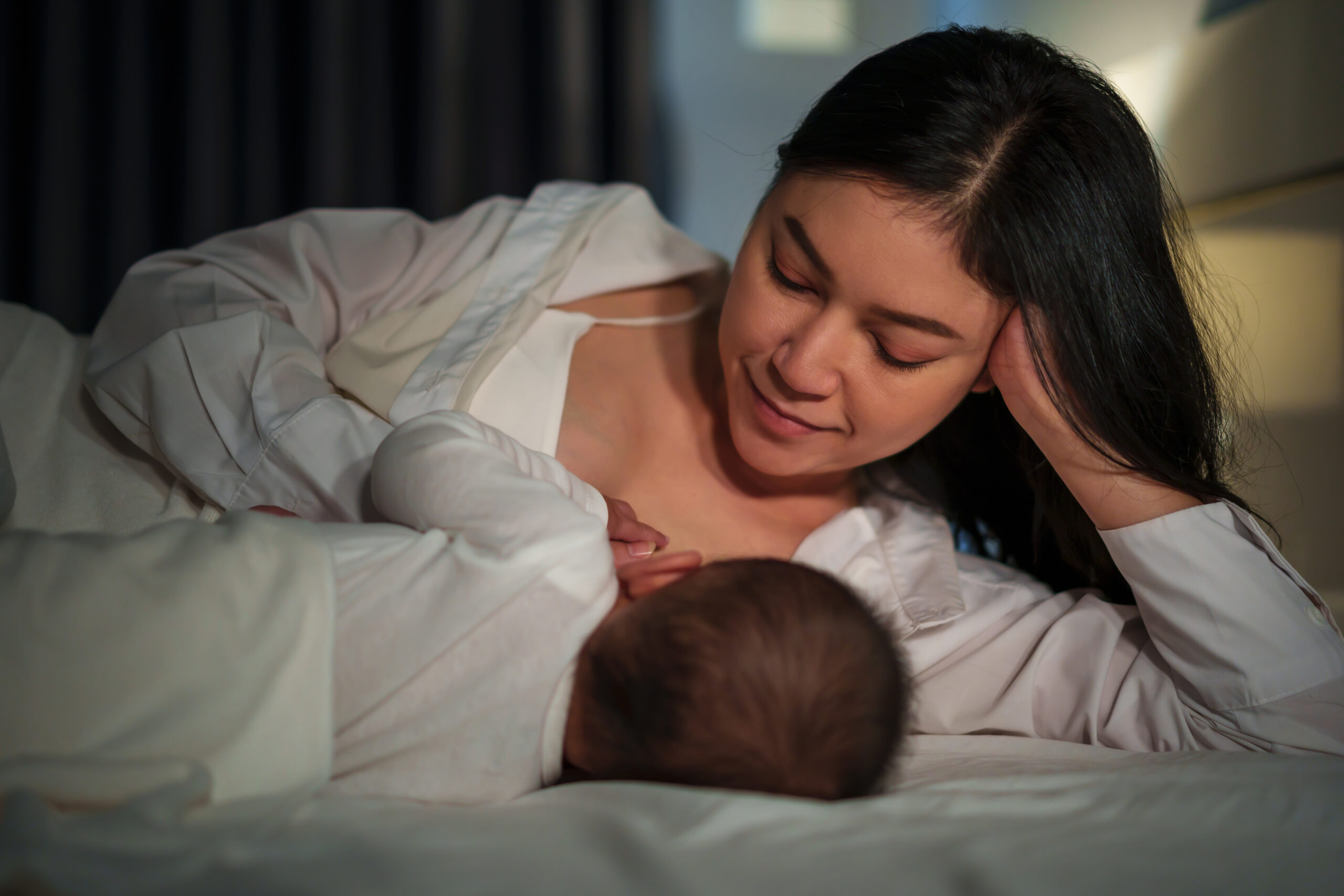mother is breastfeeding a infant baby while lying and sleeping on the bed at night