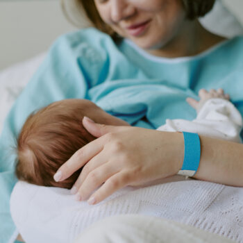 New mother in hospital gown breastfeeding newborn baby while holding closely. Both mother and baby are sharing a tender bonding moment