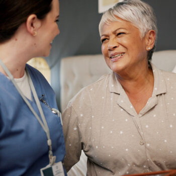Healthcare, senior woman and caregiver in nursing home, talking and care for elderly patient with Alzheimer. Happy, recovery and old person in bedroom for rehabilitation, smile and bonding with nurse