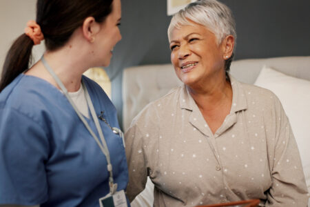 Healthcare, senior woman and caregiver in nursing home, talking and care for elderly patient with Alzheimer. Happy, recovery and old person in bedroom for rehabilitation, smile and bonding with nurse