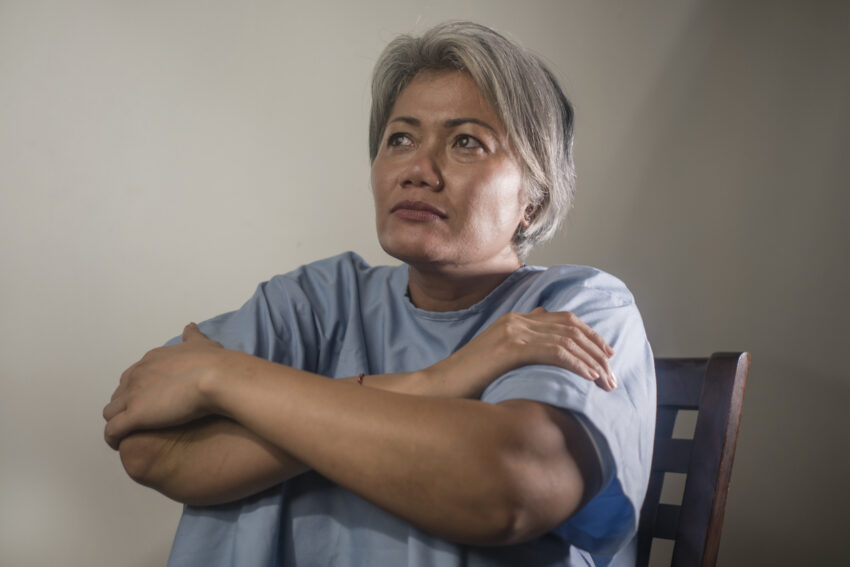 dramatic portrait of attractive sad and depressed mature woman with grey hair in pain suffering mental disorder or depression problem wearing patient gown feeling sick and abandoned