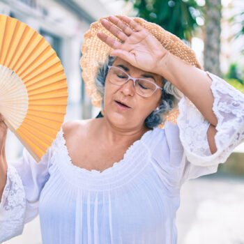 Middle age woman with grey hair using handfan on a very hot day of a heat wave
