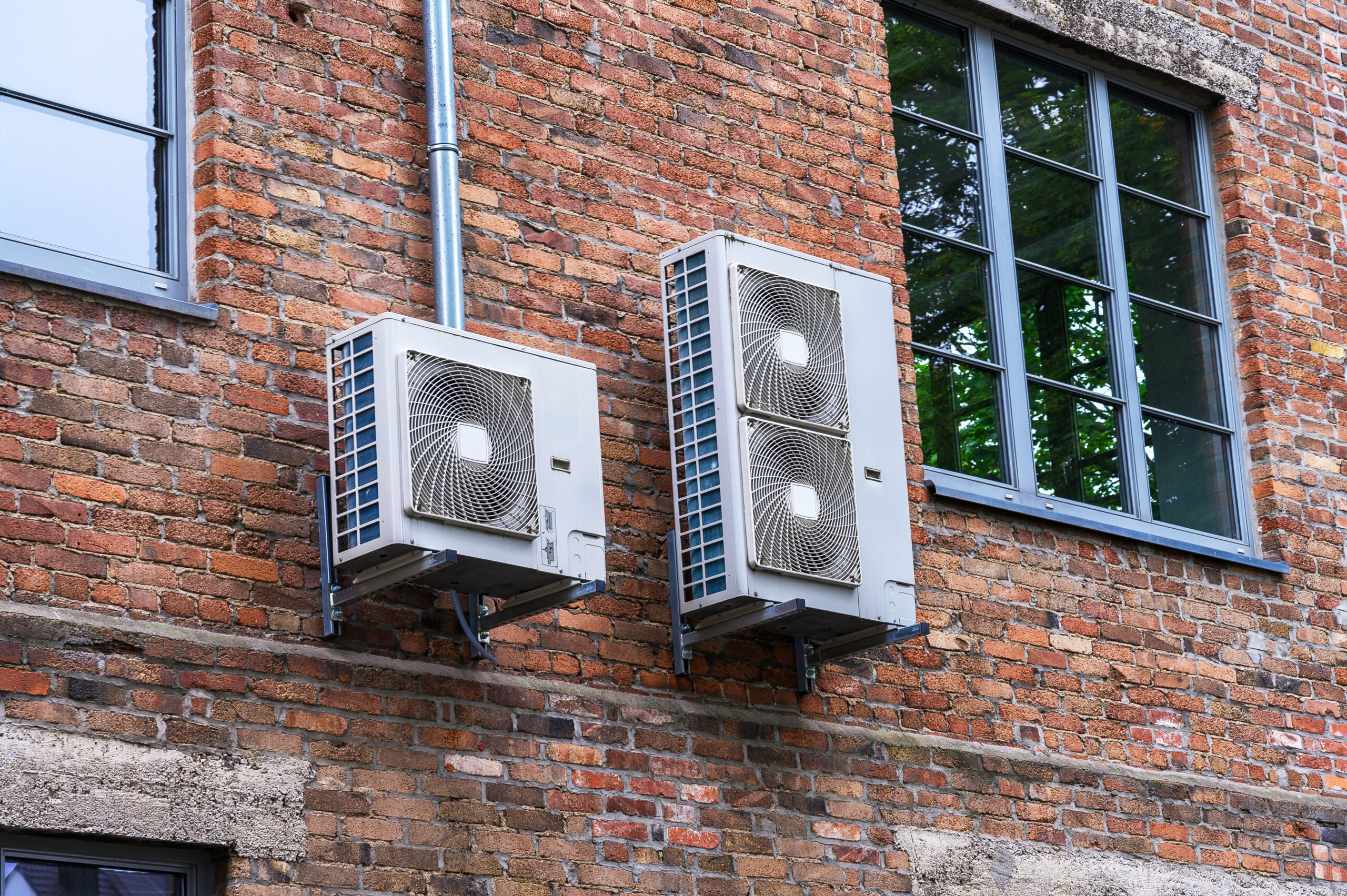 Two outdoor air conditioning units mounted on an old weathered brick building wall