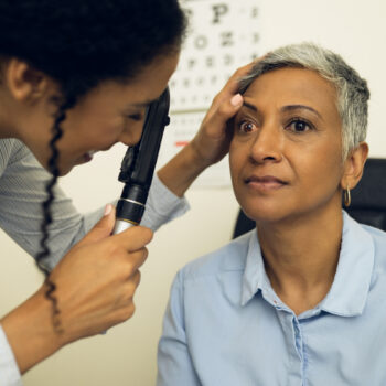 Woman, eye care and healthcare in clinic with ophthalmoscope to check for glaucoma, ocular services or assessment. Optometrist, expert and retina analysis for eyesight exam of patient with lens tools
