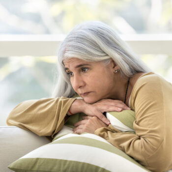 Depressed elderly woman sitting on couch with sad look away