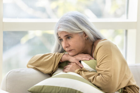 Depressed elderly woman sitting on couch with sad look away