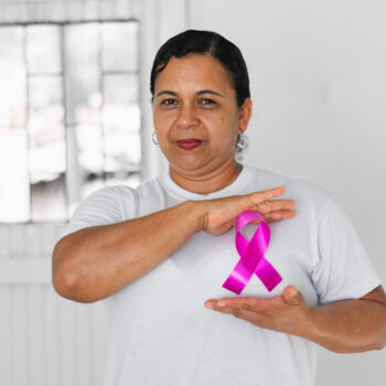 brunette latin adult woman, showing the pink ribbon that she wears on her chest as a symbol of the fight against cancer